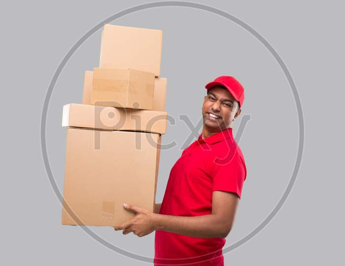 Delivery Man Holding A Lot Carton Boxes Isolated. Indian Delivery Boy Overloaded With Boxes Smilling. Heavy Boxes