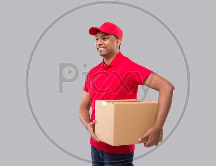 Delivery Man Holding Box In Hands Isolated. Red Tshirt Indian Delivery Boy Watching Side. Home Delivery. Quarantine Hero.