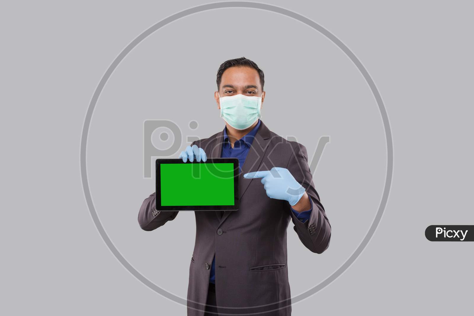 Businessman Pointing At Tablet Green Screen Wearing Medical Mask And Gloves Isolated. Indian Business Man With Tablet In Hands. Online Business Concept