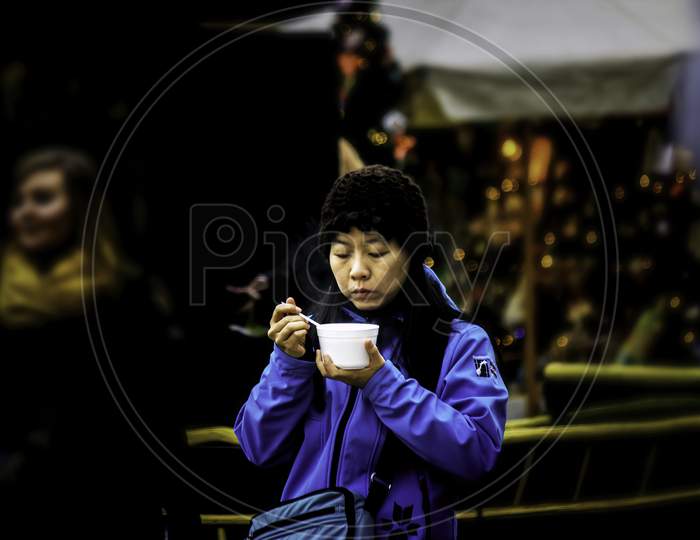 Krakow, Poland - December 08, 2014: Street Photography Of An Asian Female Enjoying Her Soup In Main Square Center Around Souvenir Shops