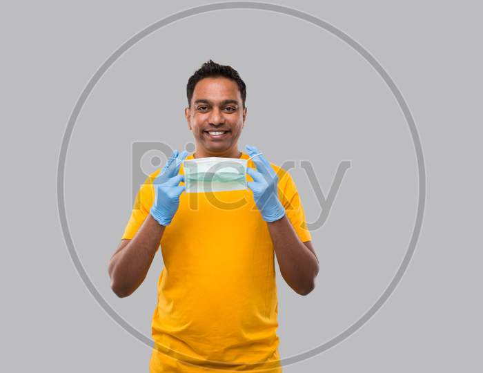 Indian Man Puts On Medical Mask And Gloves In Yellow Tshirt Isolated