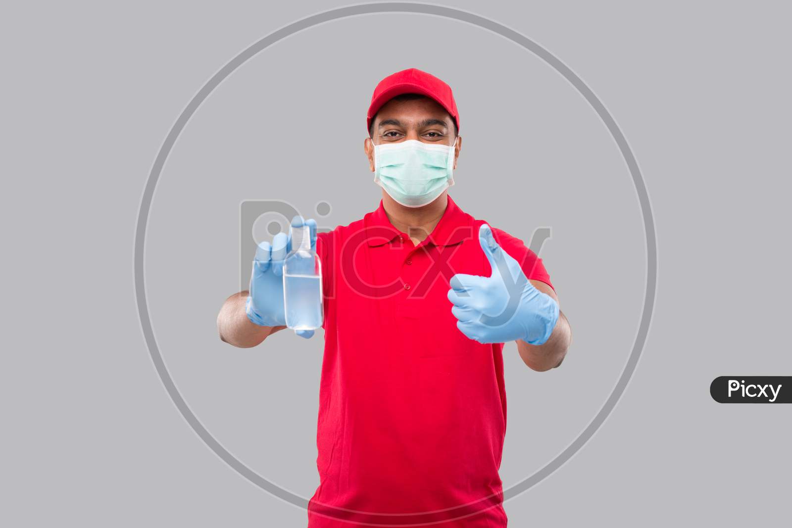 Delivery Man Showing Hands Sanitizer And Thumb Up Wearing Medical Mask And Gloves Isolated. Indian Delivery Boy Holding Hand Antiseptic