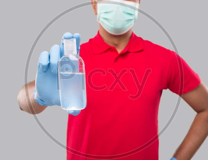 Delivery Man Showing Hands Sanitizer Wearing Medical Mask And Gloves Isolated. Indian Delivery Boy Holding Hand Antiseptic Close Up