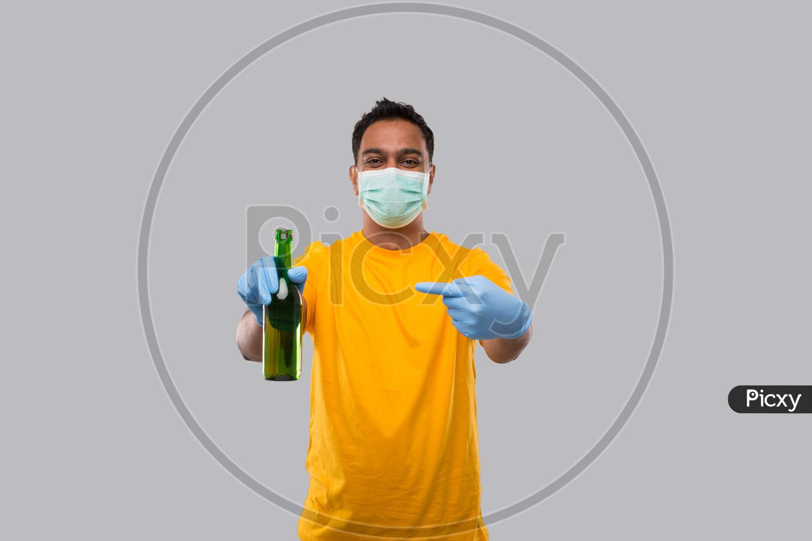 Indian Man Pointing At Beer Bottle Wearing Medical Mask And Gloves Isolated.