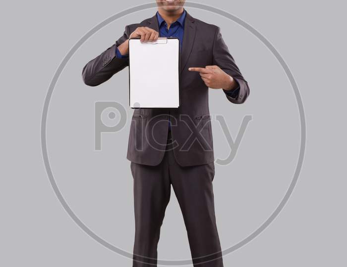 Businessman Pointing At Clipboard Watching In Camera Isolated. Indian Business Man Standing Full Length With Clipboard In Hands