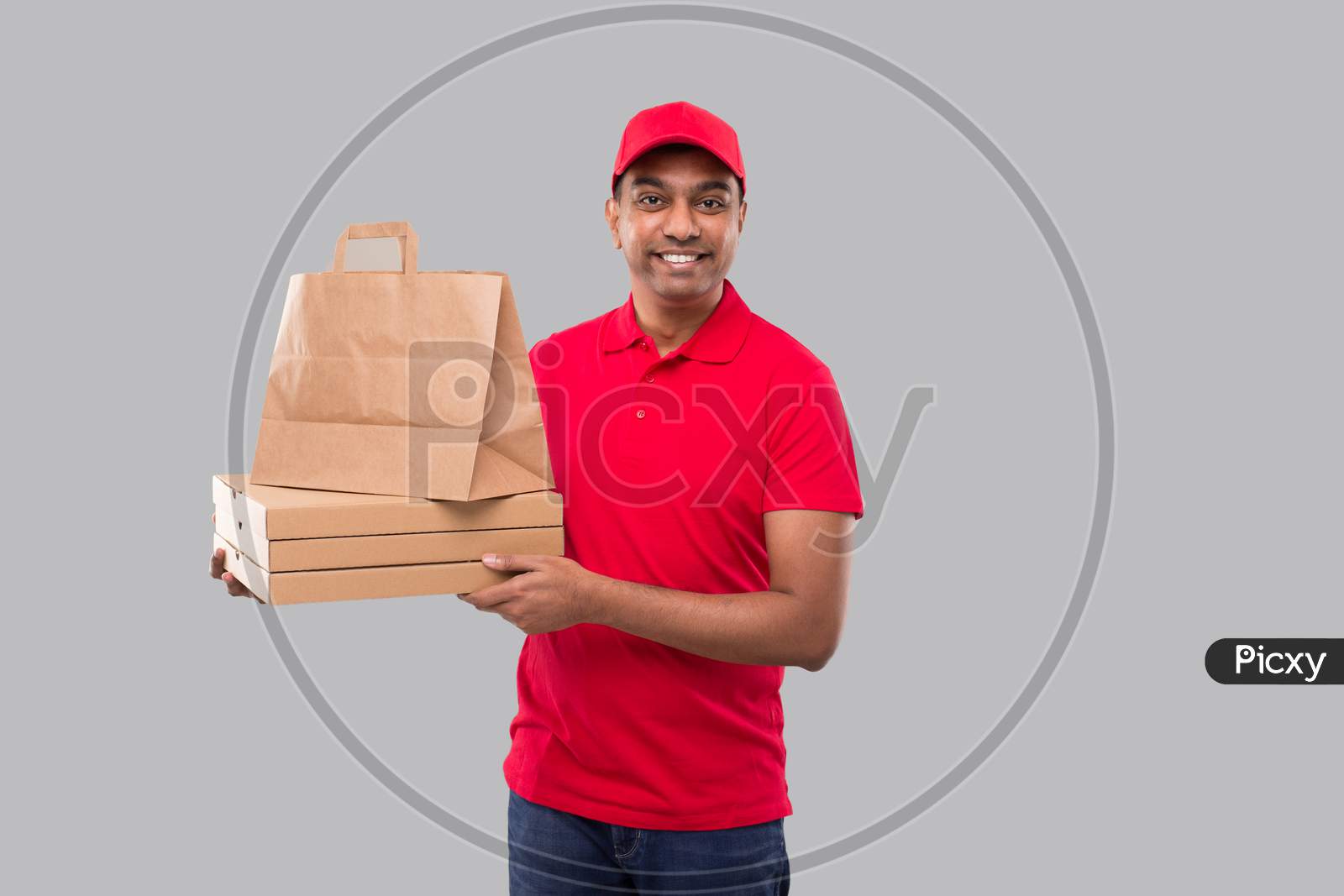 Delivery Man With Paper Bag And Three Pizza Box In Hands Isolated. Red Uniform Indian Delivery Boy. Home Food Delivery. Paper Bag