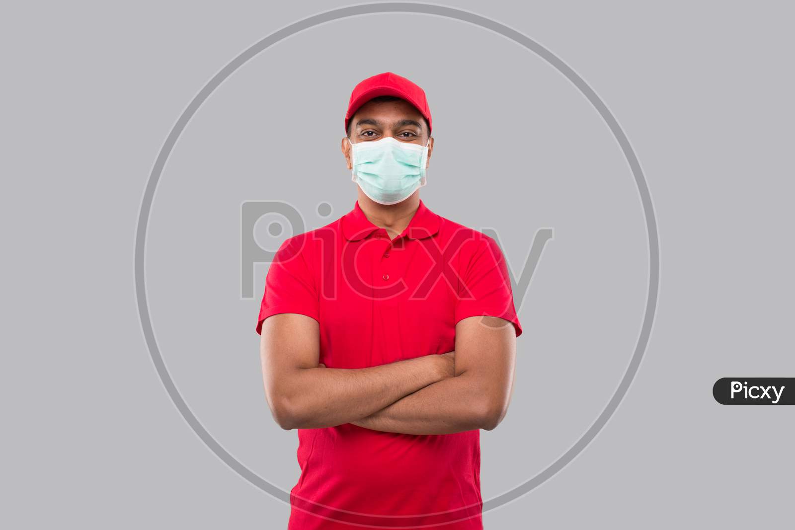 Delivery Man Standing Hands Crossed Wearing Medical Mask Isolated. Indian Delivery Boy In Red Uniform