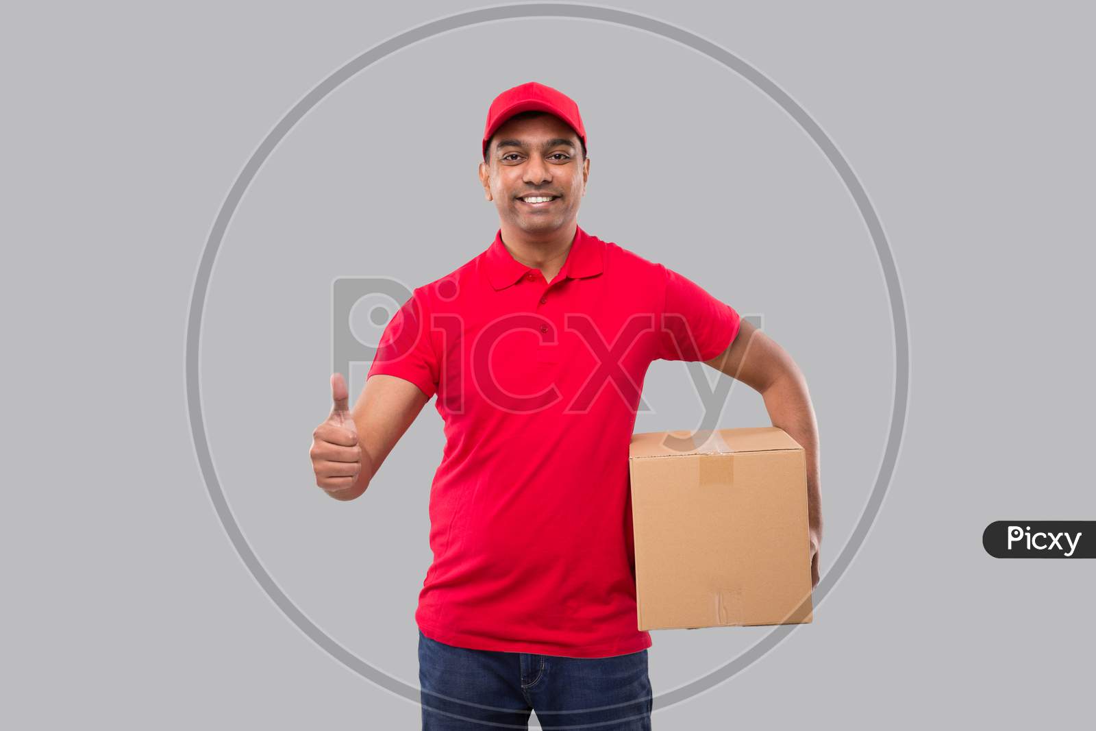 Delivery Man Holding Box In Hands Showing Thumb Up Isolated. Red Tshirt Indian Delivery Boy. Home Delivery. Quarantine Hero.