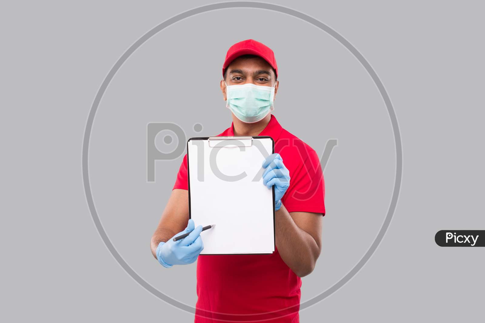 Delivery Man Pointing At Clipboard Wearing Medical Mask And Gloves Watching In Camera. Indian Delivery Boy Clipboard