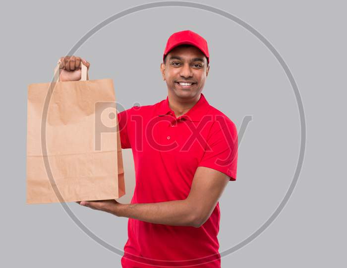 Delivery Man With Paper Bag In Hands Isolated. Red Uniform Indian Delivery Boy. Home Food Delivery. Paper Bag