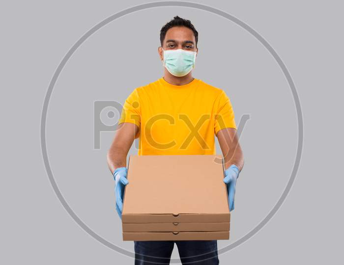 Delivery Man Three Pizza Box In Hands Wearing Medical Mask And Gloves Isolated. Yellow Tshirt Indian Delivery Boy. Man With Pizza In Hands