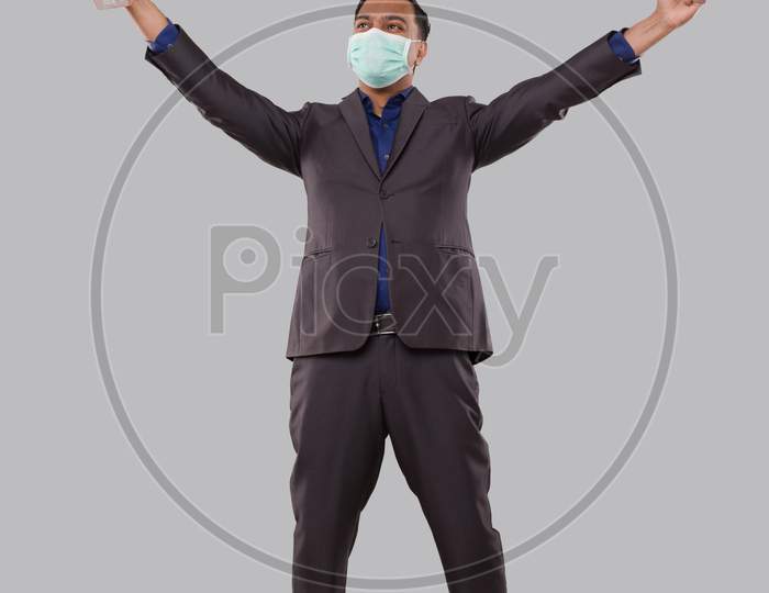 Businessman Very Happy And Excited, Raising Arms, Celebrating A Victory Or Success Holding Trophy Wearing Medical Mask. Winner Sign. Indian Business Man Isolated With Trophy In Hands