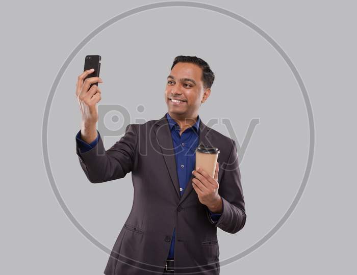 Businessman Video Call On Phone With Coffee To Go Cup Isolated. Indian Business Man With Coffee Take Away Cup