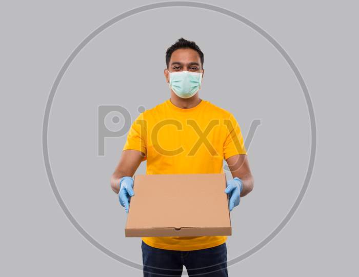 Delivery Man Pizza Box In Hands Wearing Medical Mask And Gloves Isolated. Yellow Tshirt Indian Delivery Boy. Man With Pizza In Hands