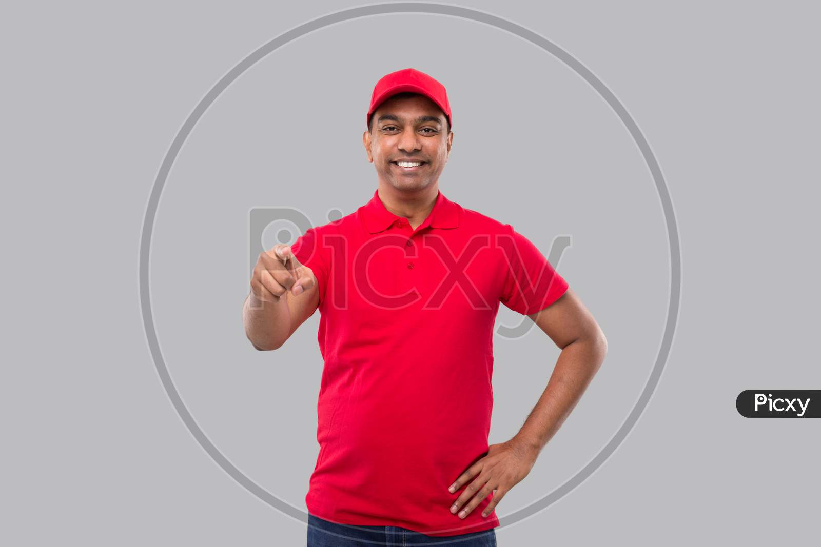 Delivery Man Pointing In Camera. Indian Delivery Boy In Red Uniform Isolated