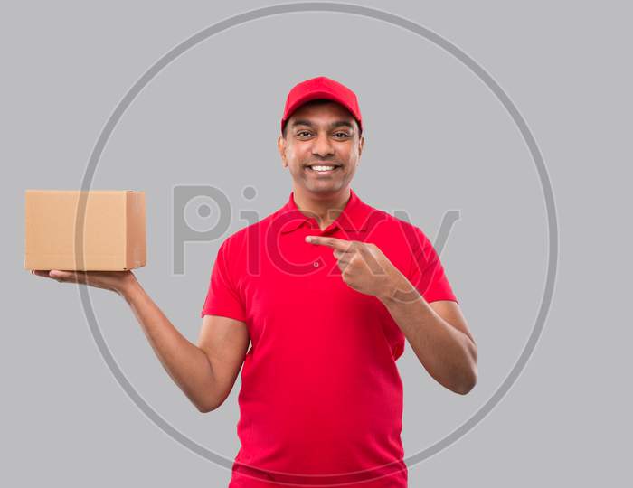 Delivery Man Pointing At Box In Hands Isolated. Red Tshirt Indian Delivery Boy. Home Delivery. Quarantine Hero.