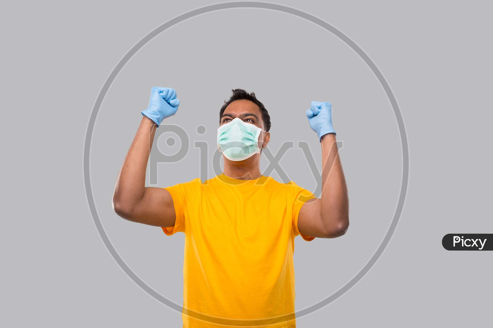 Indian Man Very Happy And Excited, Raising Arms, Celebrating A Victory Or Success Wearing Medical Mask And Gloves. Winner Sign. Indian Man Isolated