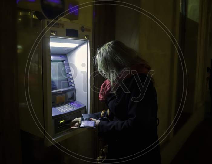 Krakow, Poland - October 25, 2014: A Woman Using Atm At Night In Winter
