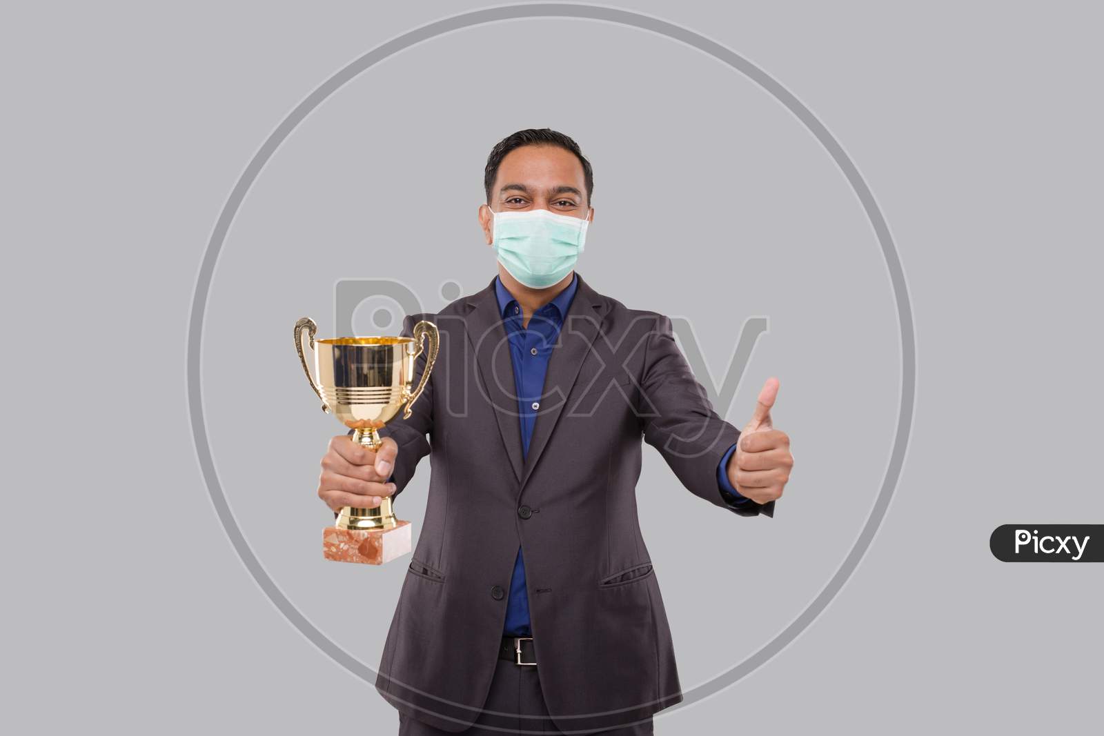 Businessman Holding Trophy Wearing Medical Mask Showing Thumbp Up. Indian Business Man Standing With Trophy In Hands
