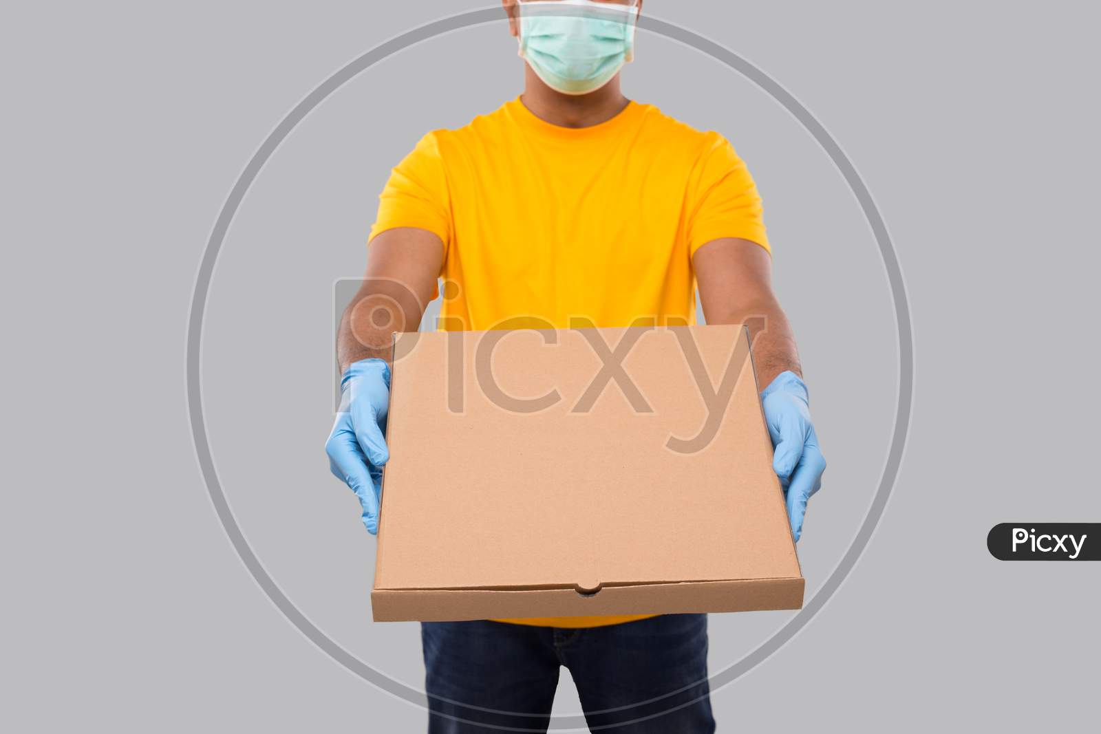 Delivery Man Pizza Box In Hands Wearing Medical Mask And Gloves Isolated Close Up. Yellow Tshirt Indian Delivery Boy. Man With Pizza In Hands