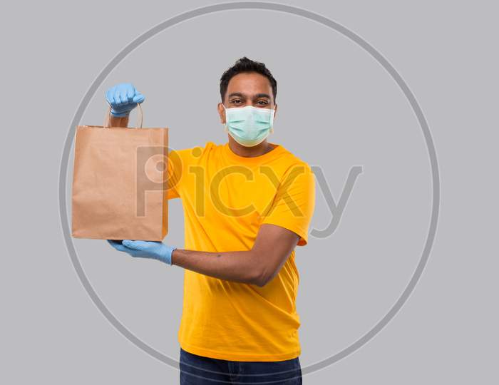 Delivery Man With Paper Bag In Hands Wearing Medical Mask And Gloves Isolated. Yellow Uniform Indian Delivery Boy. Home Food Delivery. Paper Bag