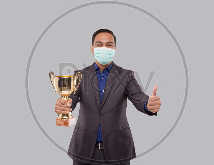Businessman Holding Trophy Wearing Medical Mask Showing Thumbp Up. Indian Business Man Standing With Trophy In Hands