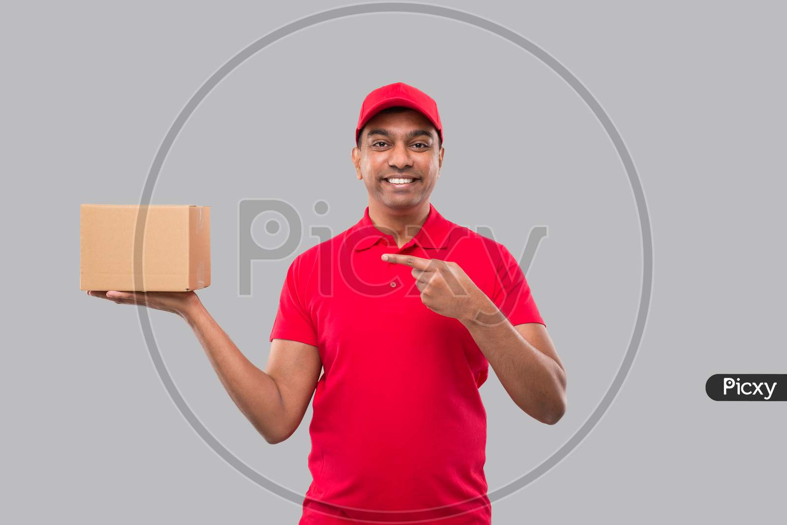 Delivery Man Pointing At Box In Hands Isolated. Red Tshirt Indian Delivery Boy. Home Delivery. Quarantine Hero.