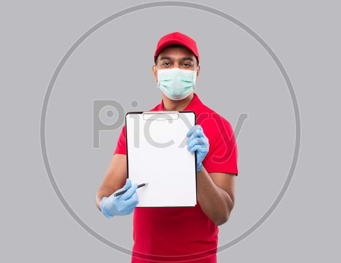 Delivery Man Pointing At Clipboard Wearing Medical Mask And Gloves Watching In Camera. Indian Delivery Boy Clipboard
