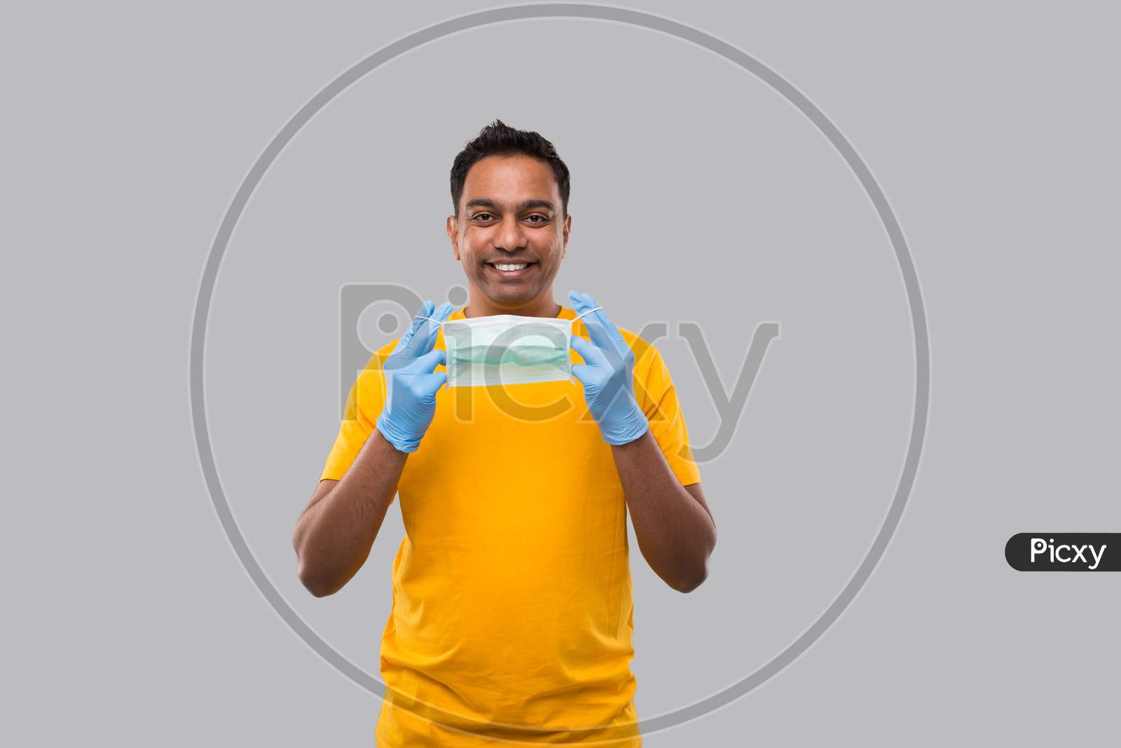 Indian Man Puts On Medical Mask And Gloves In Yellow Tshirt Isolated