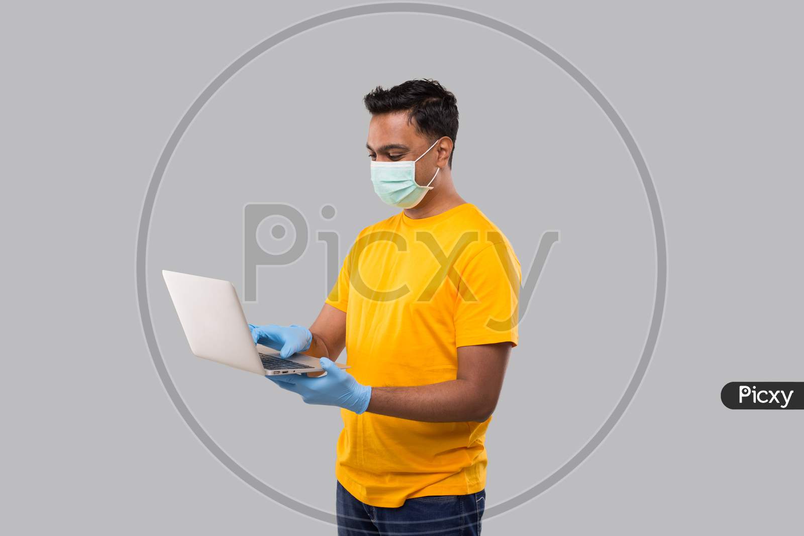 Indian Man Using Laptop Green Screen Wearing Medical Mask And Gloves. Home Orders, Quarantine Delivery, Shopping Online, Freelance Worker Concept.
