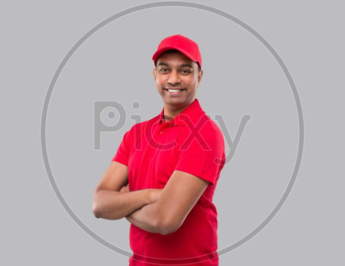Delivery Man Standing Hands Crossed Smiling. Indian Delivery Boy In Red Uniform Isolated