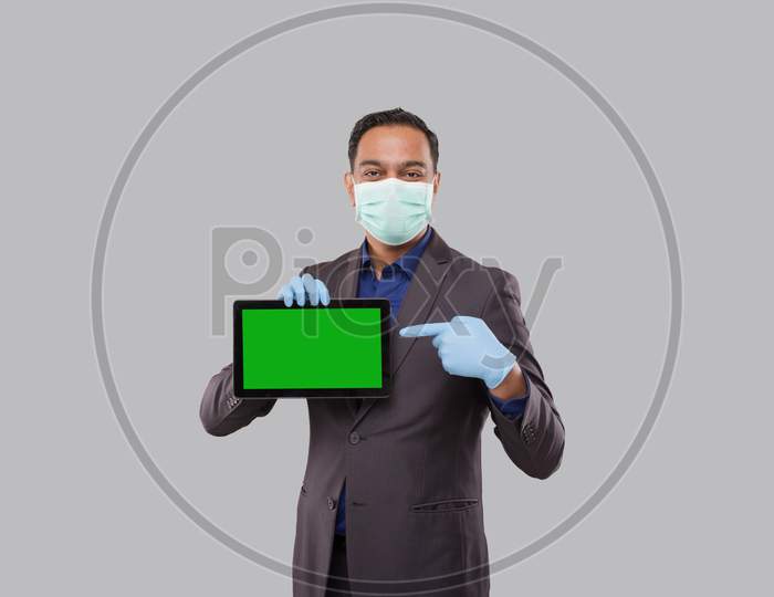 Businessman Pointing At Tablet Green Screen Wearing Medical Mask And Gloves Isolated. Indian Business Man With Tablet In Hands. Online Business Concept