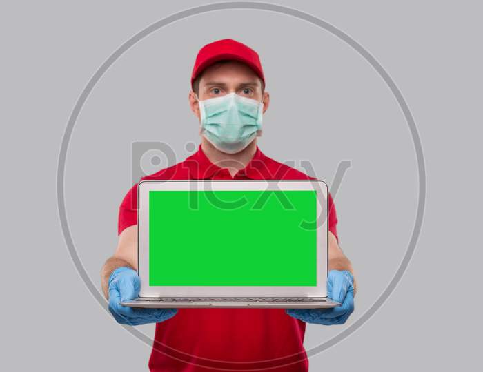 Delivery Man Wearing Medical Mask And Gloves Showing Laptop Green Screen. Home Orders, Quarantine Delivery, Shopping Online, Freelance Worker Concept.