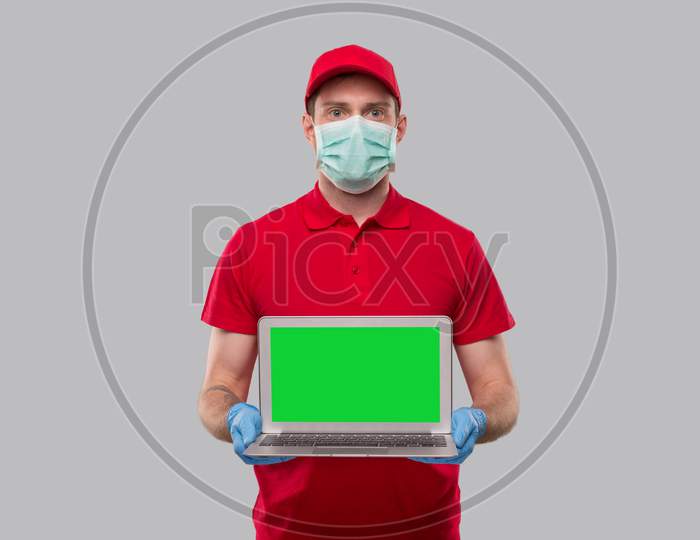 Delivery Man Wearing Medical Mask And Gloves Holding Laptop Green Screen. Home Orders, Quarantine Delivery, Shopping Online, Freelance Worker Concept.