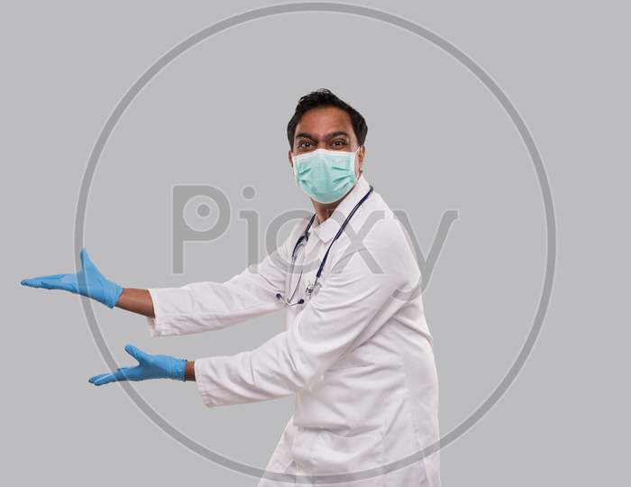 Doctor Holding Open Hands To Side Wearing Medical Mask And Gloves Watching To Camera Isolated. Indian Man Doctor Excited Sign