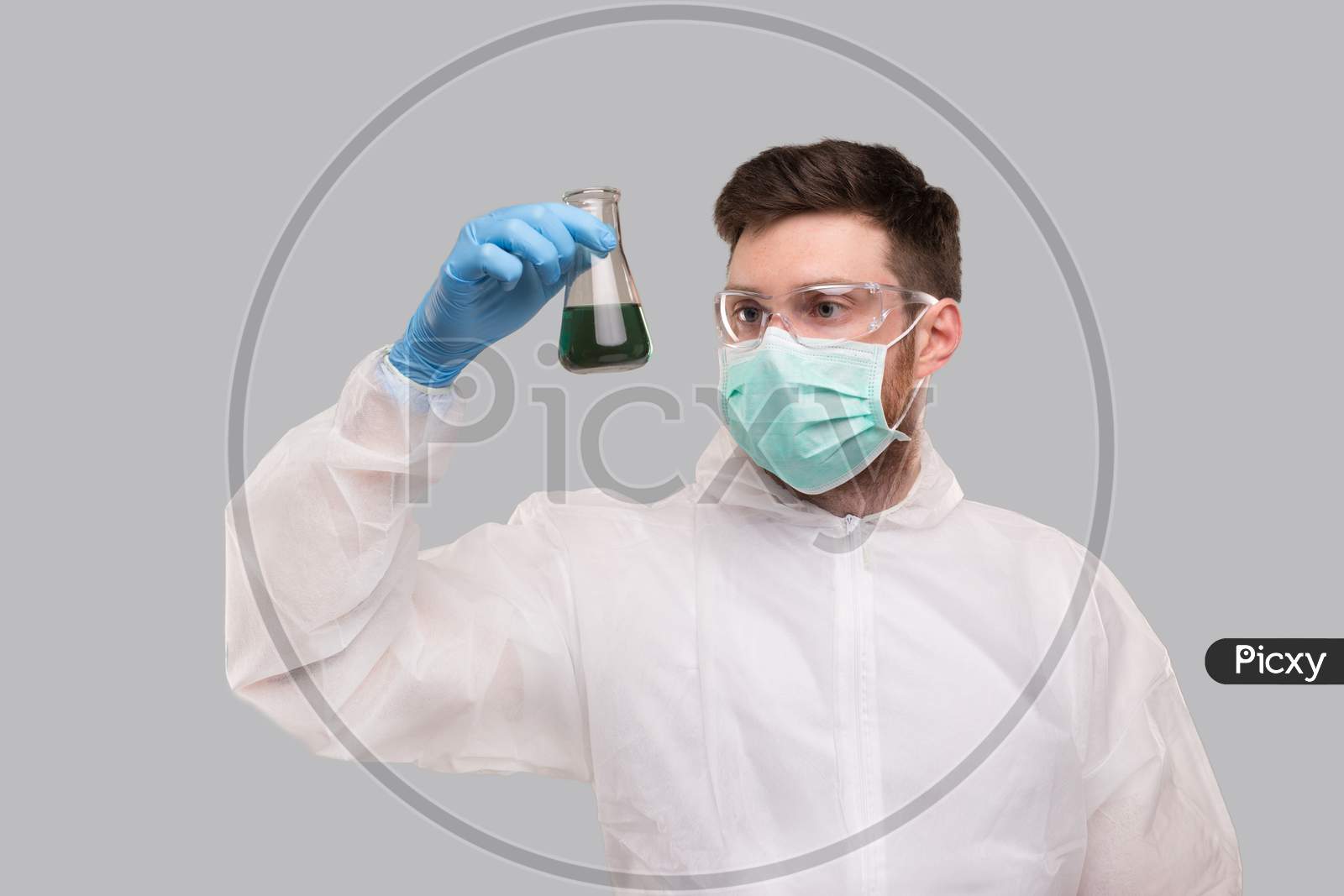 Male Laboratory Worker In Chemical Suit, Wearing Medical Mask And Glasses Watching Flask With Colorfull Liquid. Science, Medical, Virus Concept