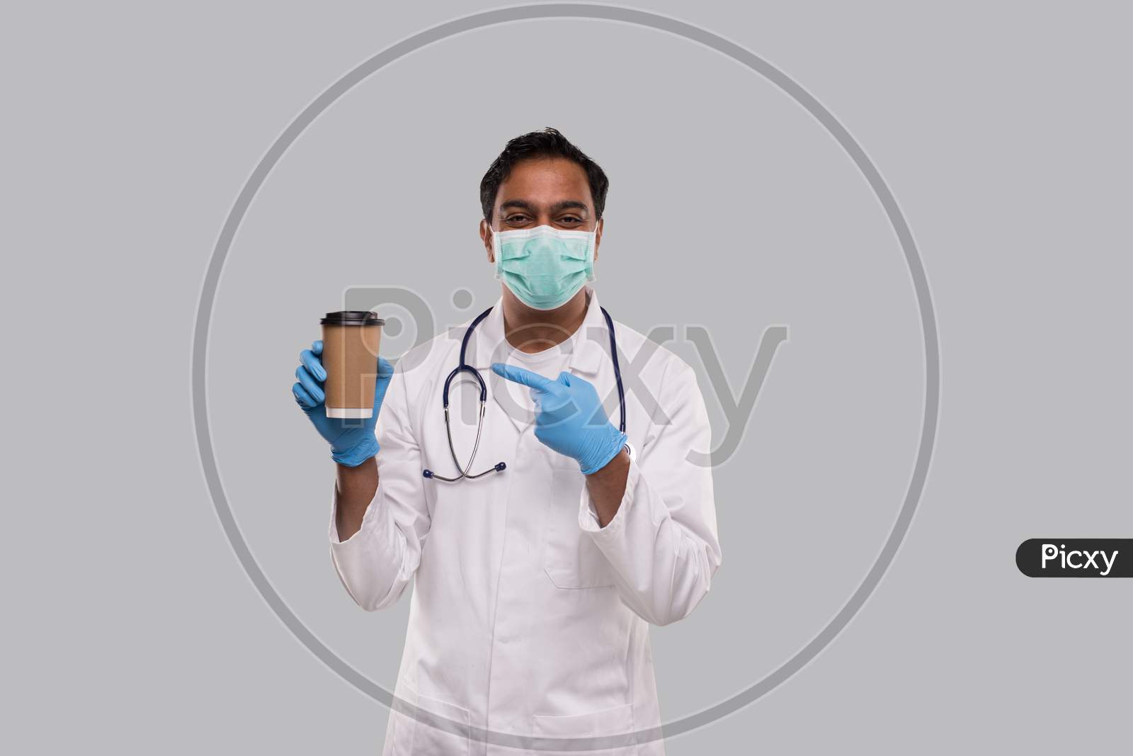 Indian Man Doctor Pointing At Coffee Take Away Cup Wearing Medical Mask And Gloves Isolated. Indian Doctor Holding Coffee To Go Cup.