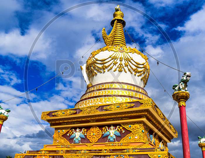 A Monument Of Buddhist Statue . It Contains Beautiful Paintings In Golden And White Color With Blue Sky Behind
