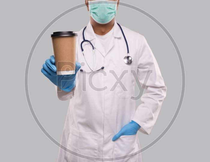 Indian Man Doctor Showing Coffee Take Away Cup Wearing Medical Mask And Gloves Close Up Isolated. Indian Doctor Holding Coffee To Go Cup.