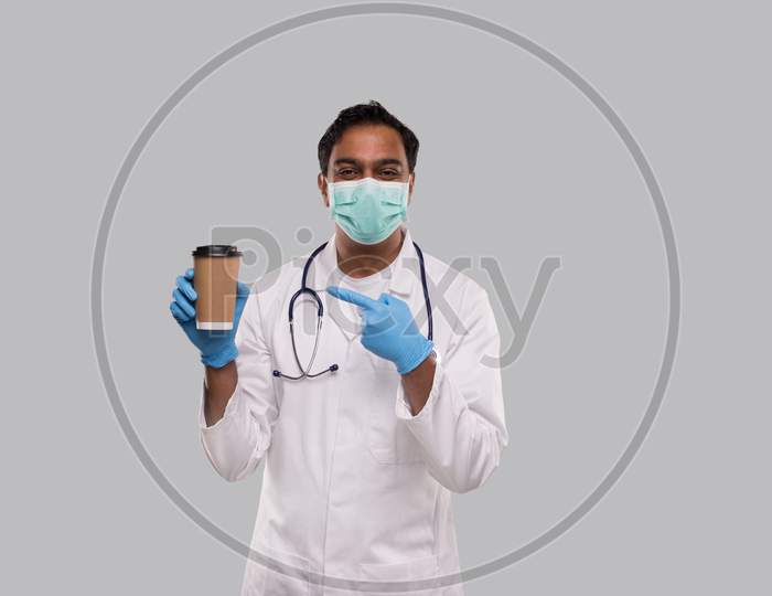 Indian Man Doctor Pointing At Coffee Take Away Cup Wearing Medical Mask And Gloves Isolated. Indian Doctor Holding Coffee To Go Cup.