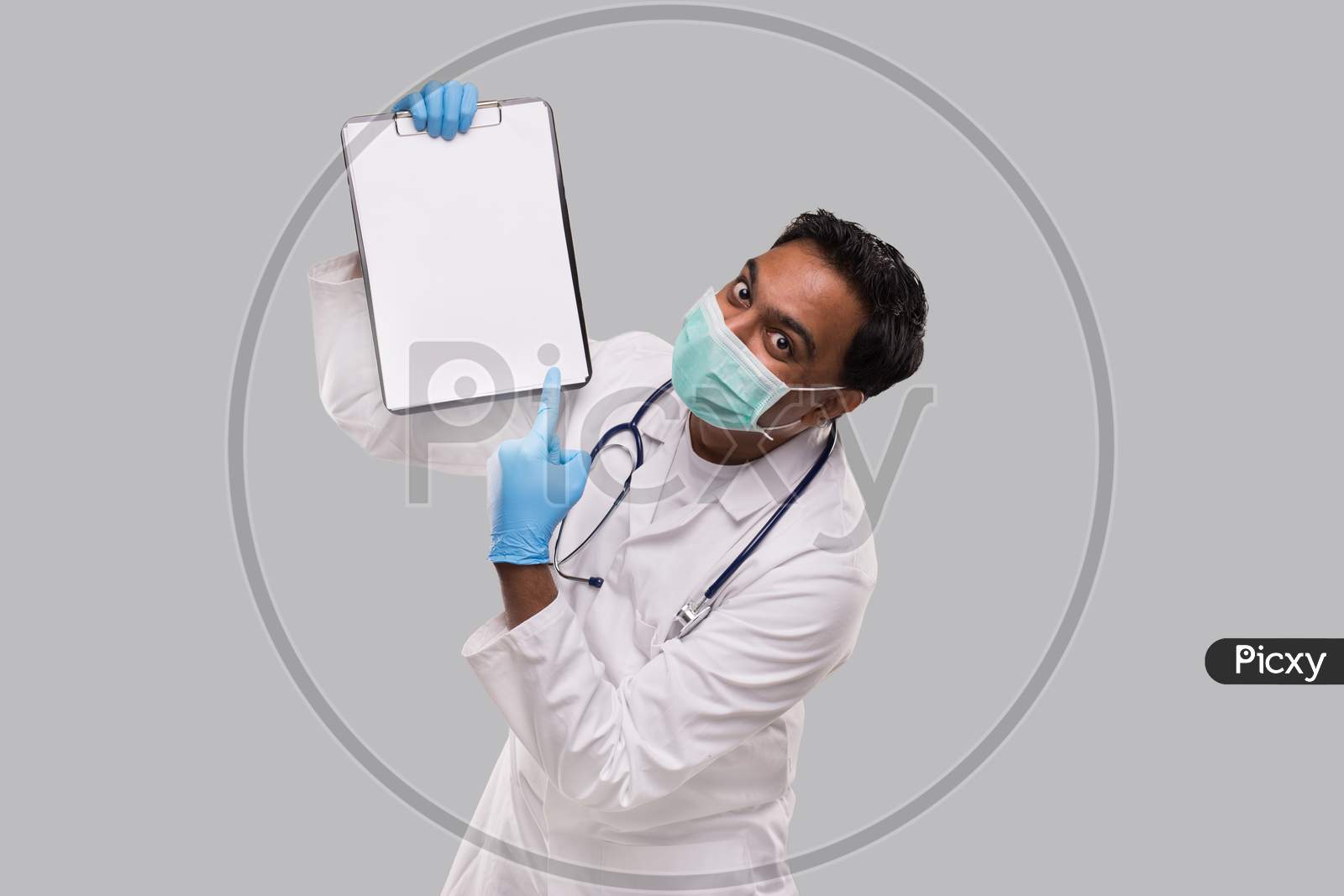 Doctor Pointing At Clipboard Wearing Medical Mask And Gloves Isolated. Indian Man Doctor Blank Clipboard In Hands