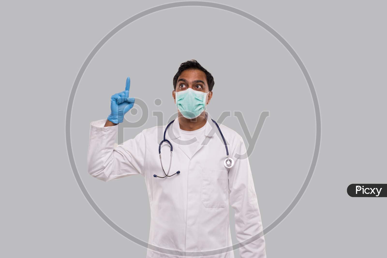 Indian Man Doctor Pointing Up And Watching Up Wearing Medical Mask And Gloves Isolated