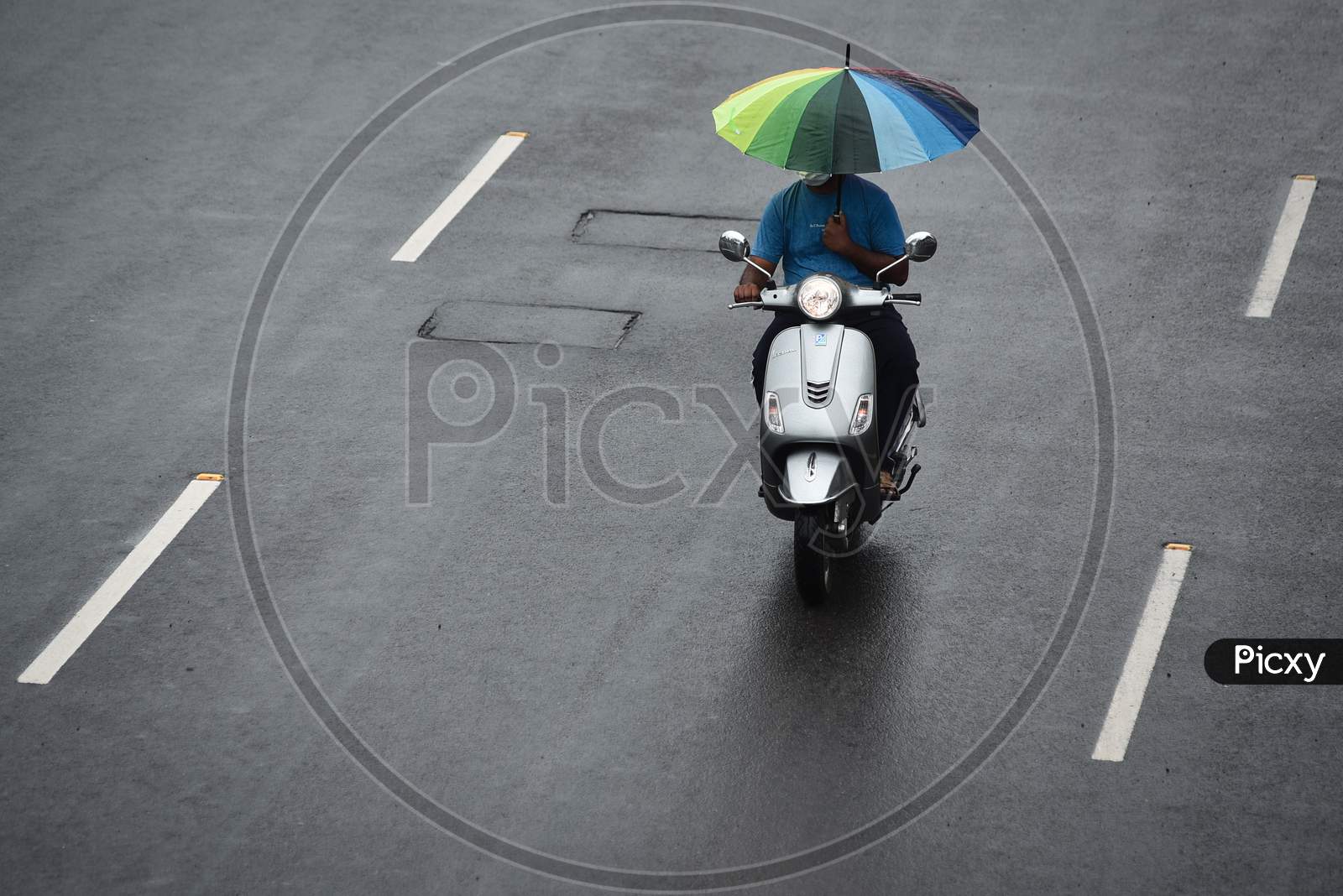 A man holds an umbrella while driving a two-wheeler on a road during rain in Vijayawada.