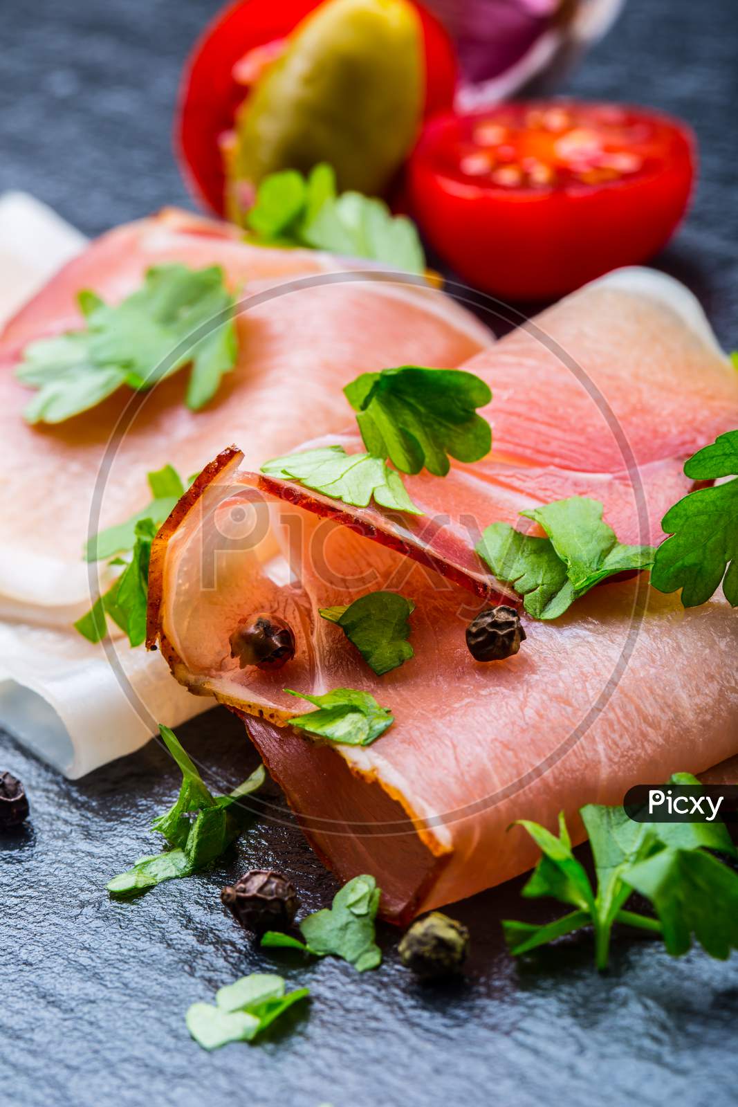 Prosciutto. Curled Slices of Delicious Prosciutto with parsley leaves on granite board. Prosciuto with spice cherry tomatoes garlic and olive. Italian and Mediterranean cuisine