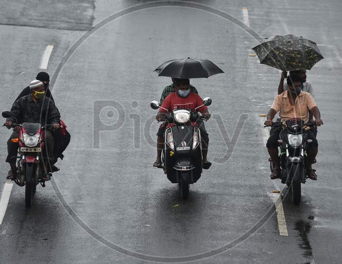 People cover themselves with umbrellas while driving on a road during rain in Vijayawada.