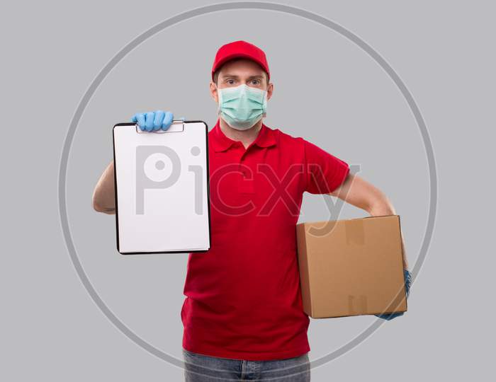 Delivery Man Wearing Medical Mask And Gloves Holding Clipboard And Box In Hands. Blank Clipboard In Hands