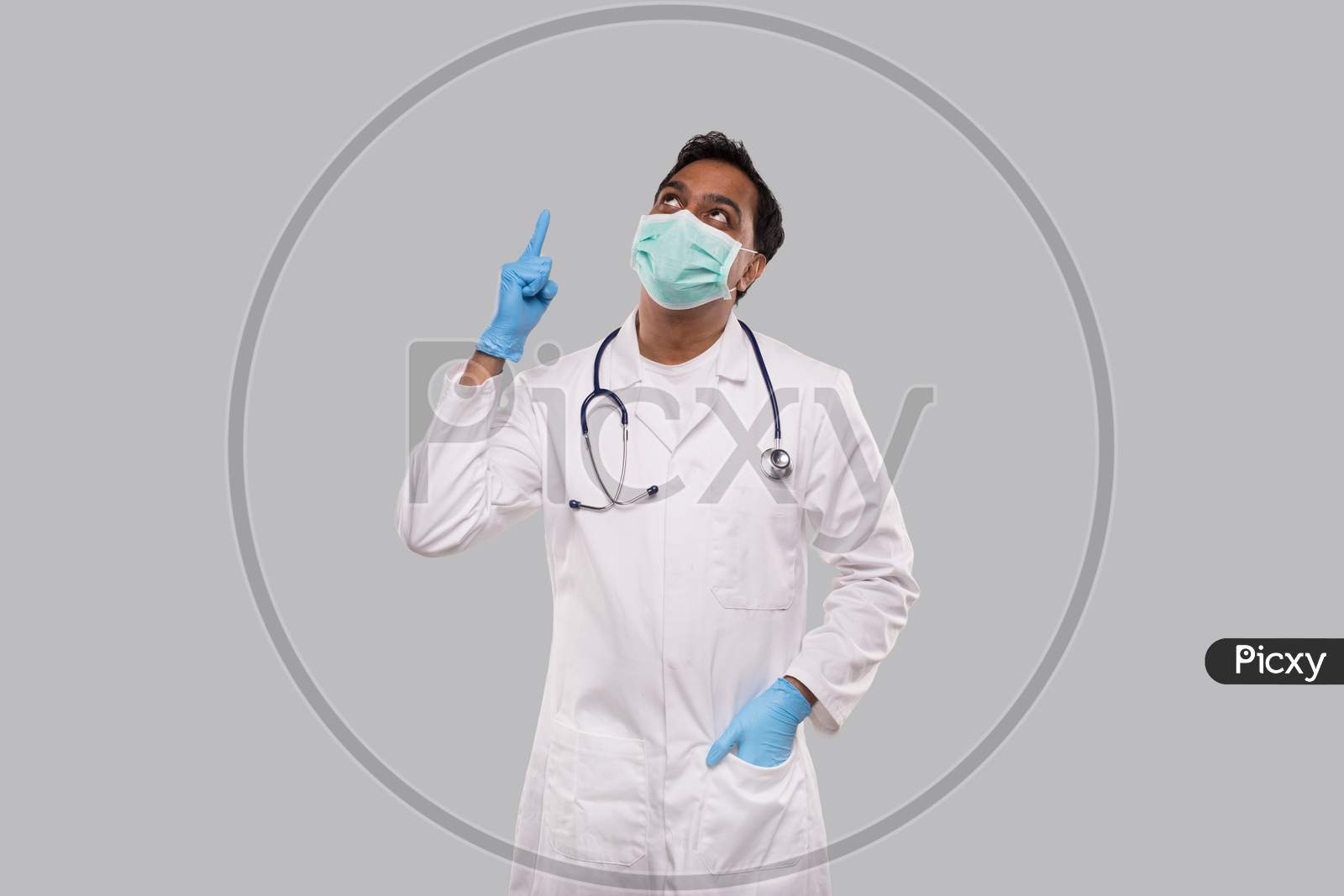 Doctor Pointing Up And Watching Up Wearing Medical Mask And Gloves Isolated. Indian Man Doctor Good Idea.
