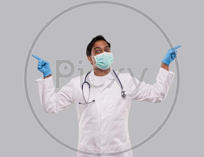 Indian Man Doctor Pointing To Sides Both Hands Wearing Medical Mask And Gloves. Isolated