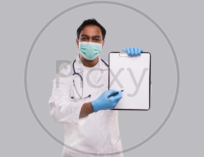 Doctor Pointing At Clipboard With Pen Wearing Medical Mask And Gloves Isolated. Indian Man Doctor Blank Clipboard In Hands