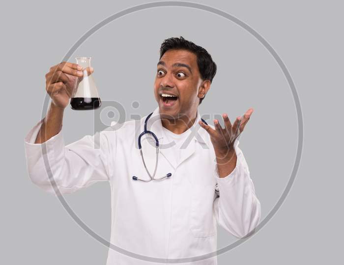 Male Doctor Excited Watching Flask With Colorfull Liquid Isolated. Science, Medical, Virus Concept. Indian Man Doctor Smilling.